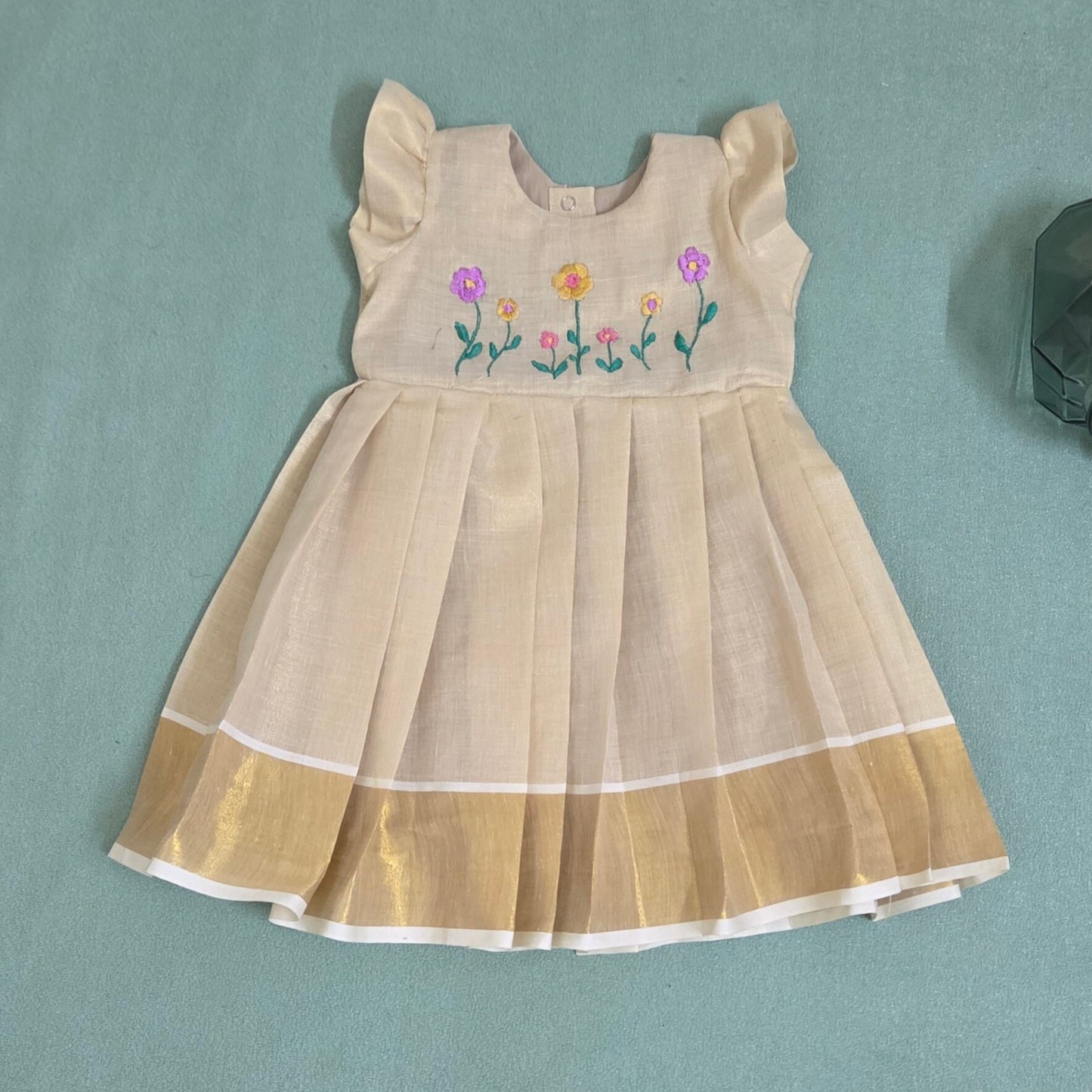 onam Beige dress with floral embroidery and kasavu border on green bac ground