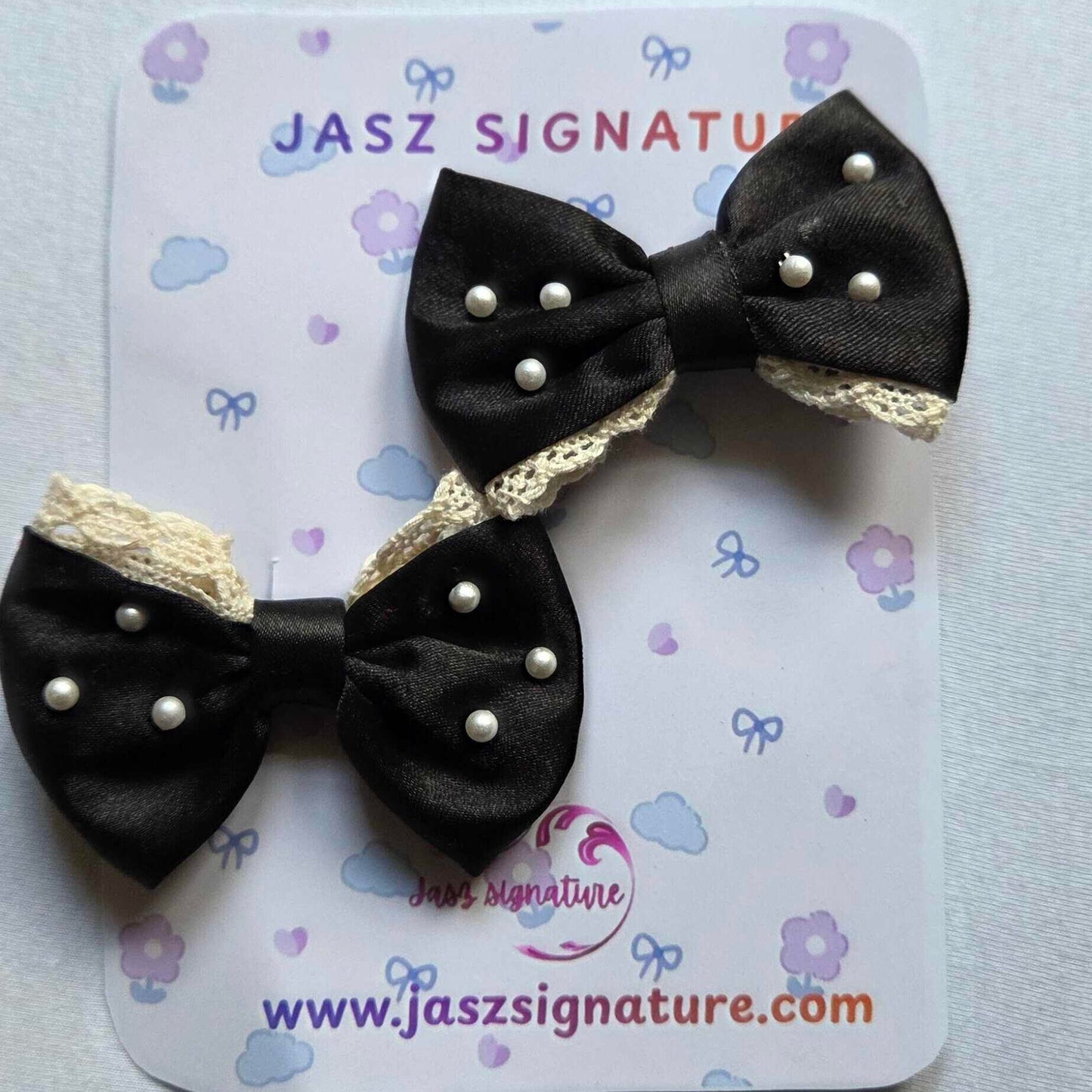 Black bow hair clips with gold accents on a Jasz Signature card.