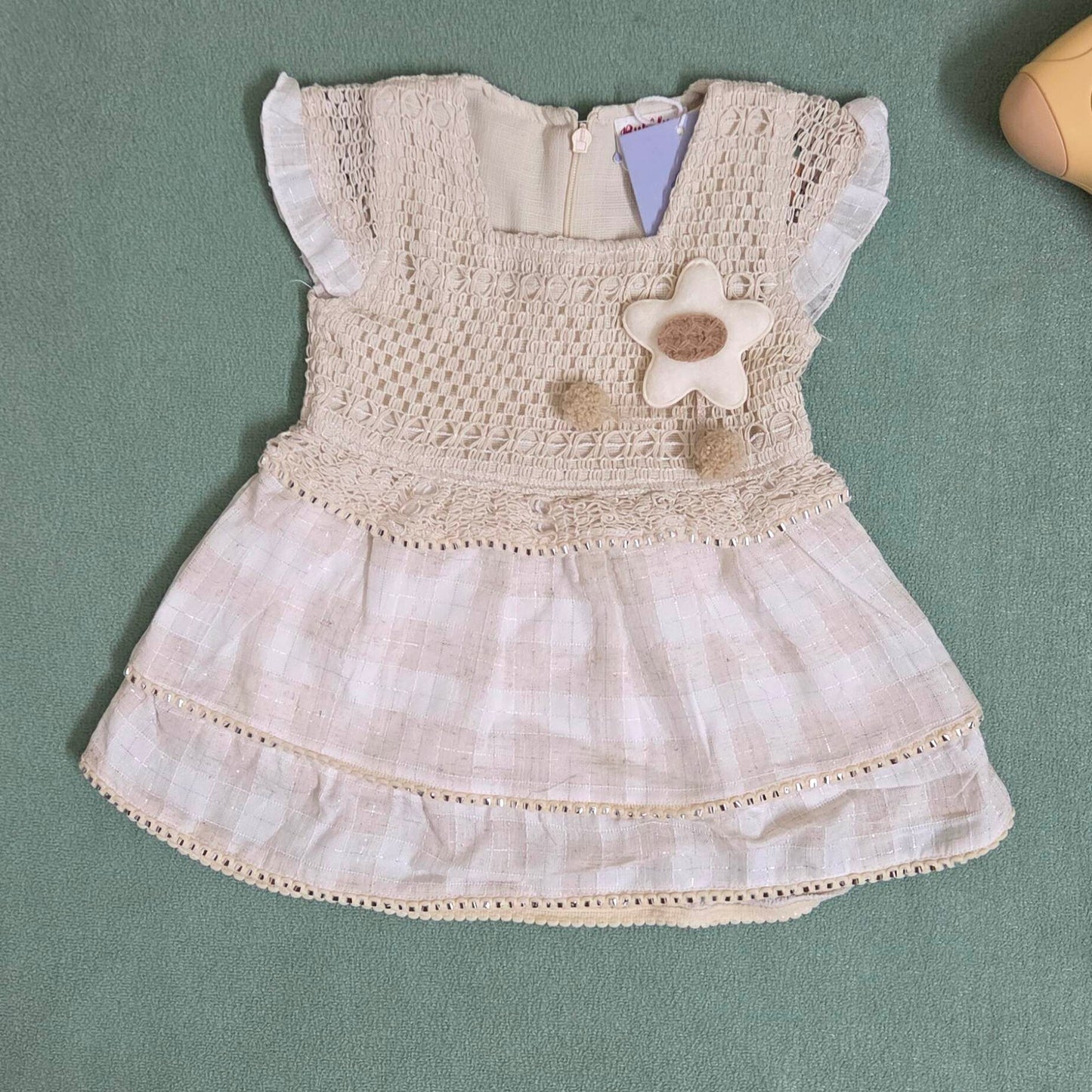 Beige baby dress with floral details on a green surface