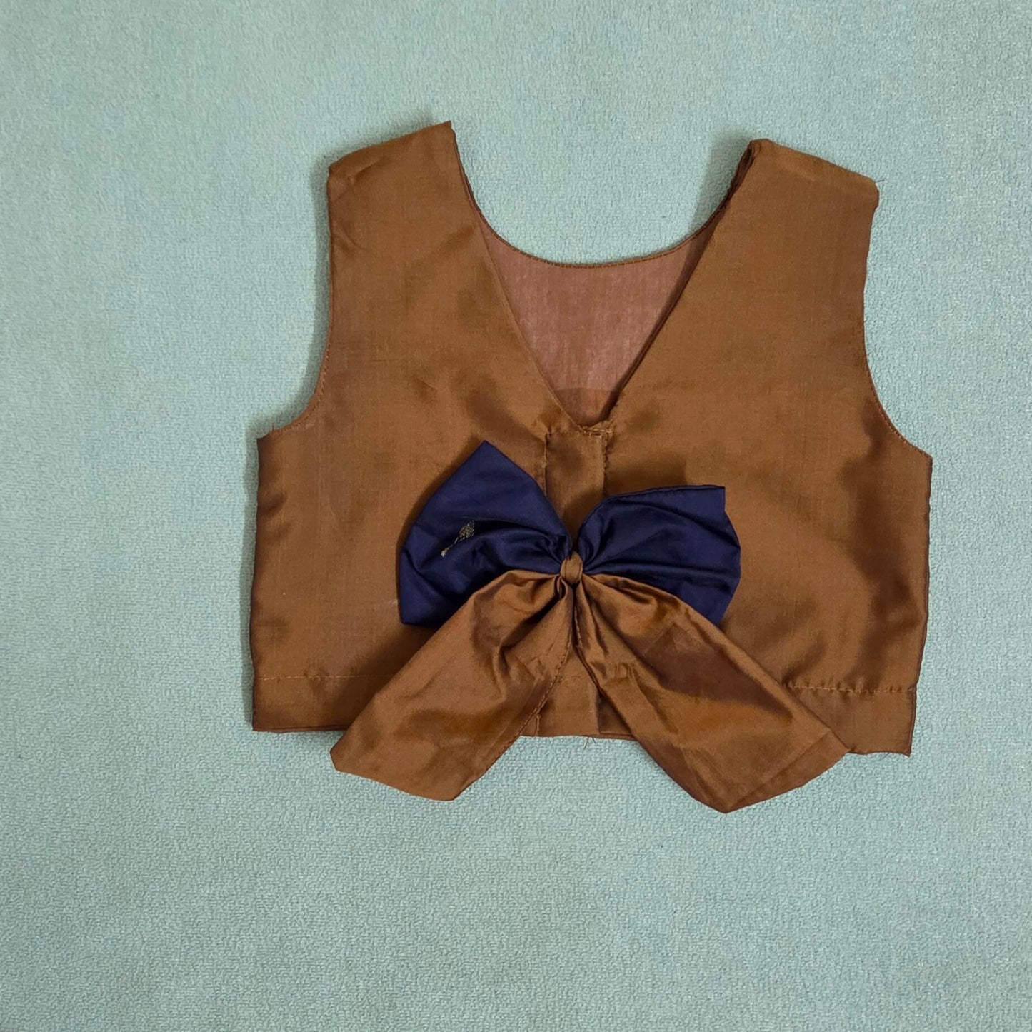 Brown vest with a large blue bow on a light gray background