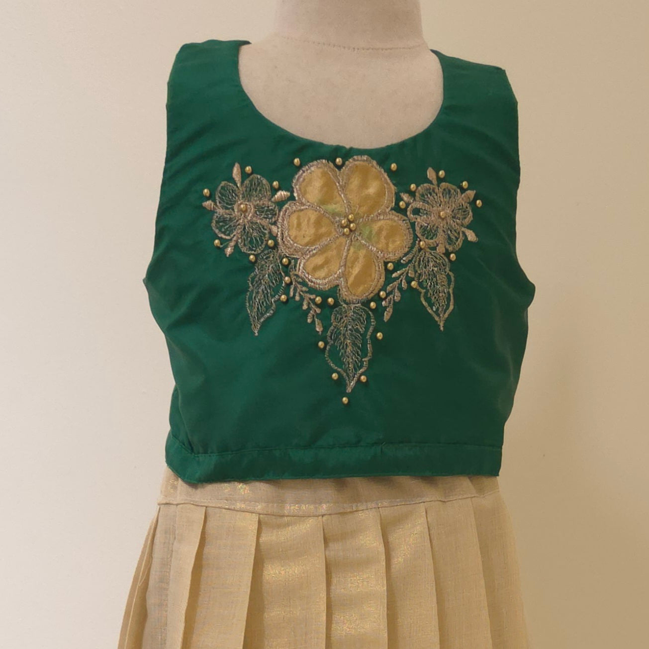 Green top with floral embroidery on a mannequin against a beige background