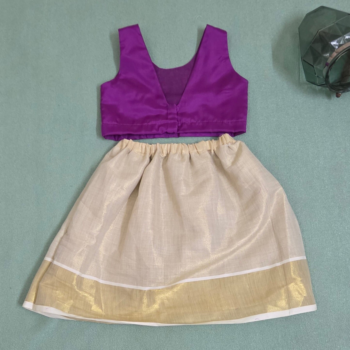 Purple top and beige skirt with gold border on a green background