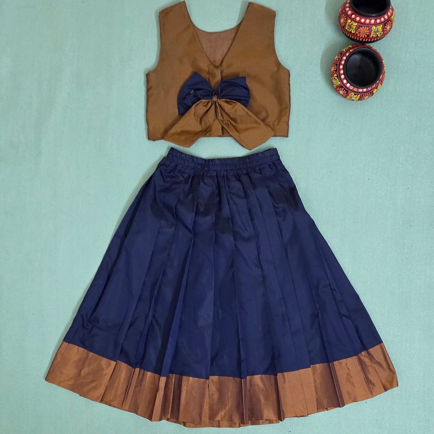 Brown top with a large blue bow and matching brown hem on a blue skirt, on a light blue background.