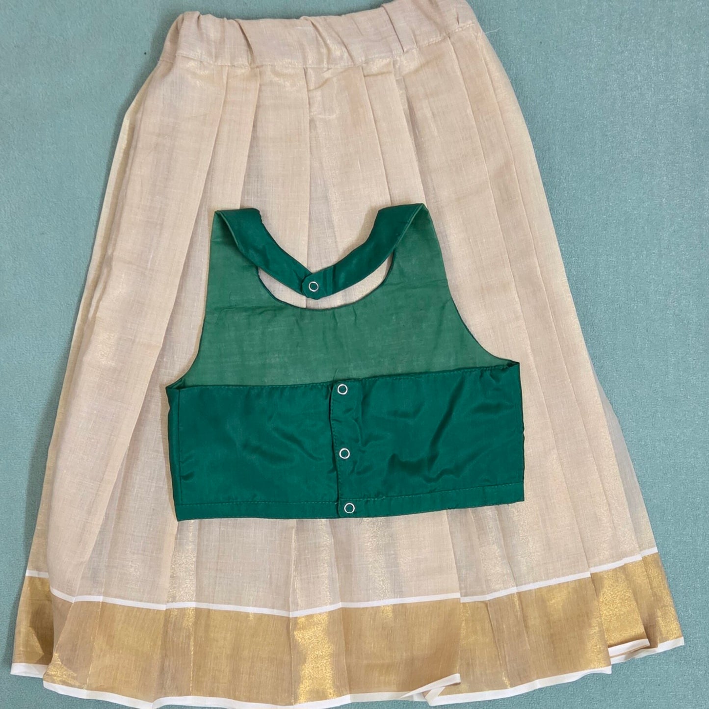 Green top with beige and gold skirt on a light blue background