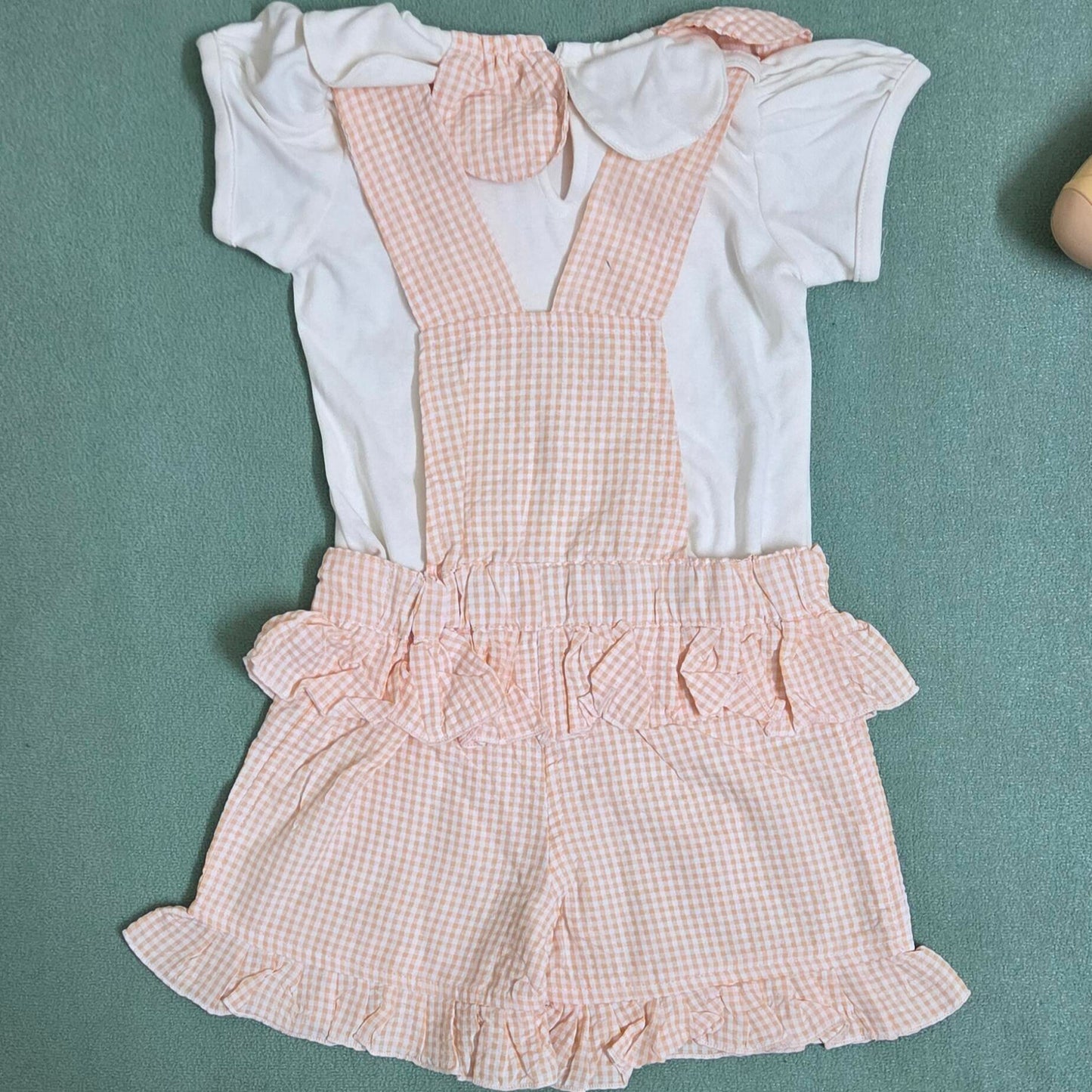 Children's outfit with pink checkered romper and white shirt on a green background