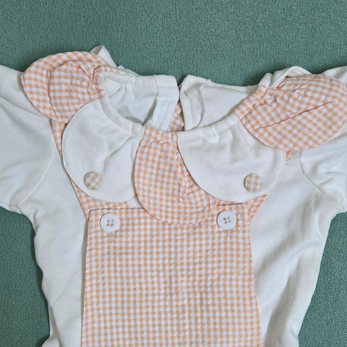 Baby romper with checkered pattern and white collar on a green surface
