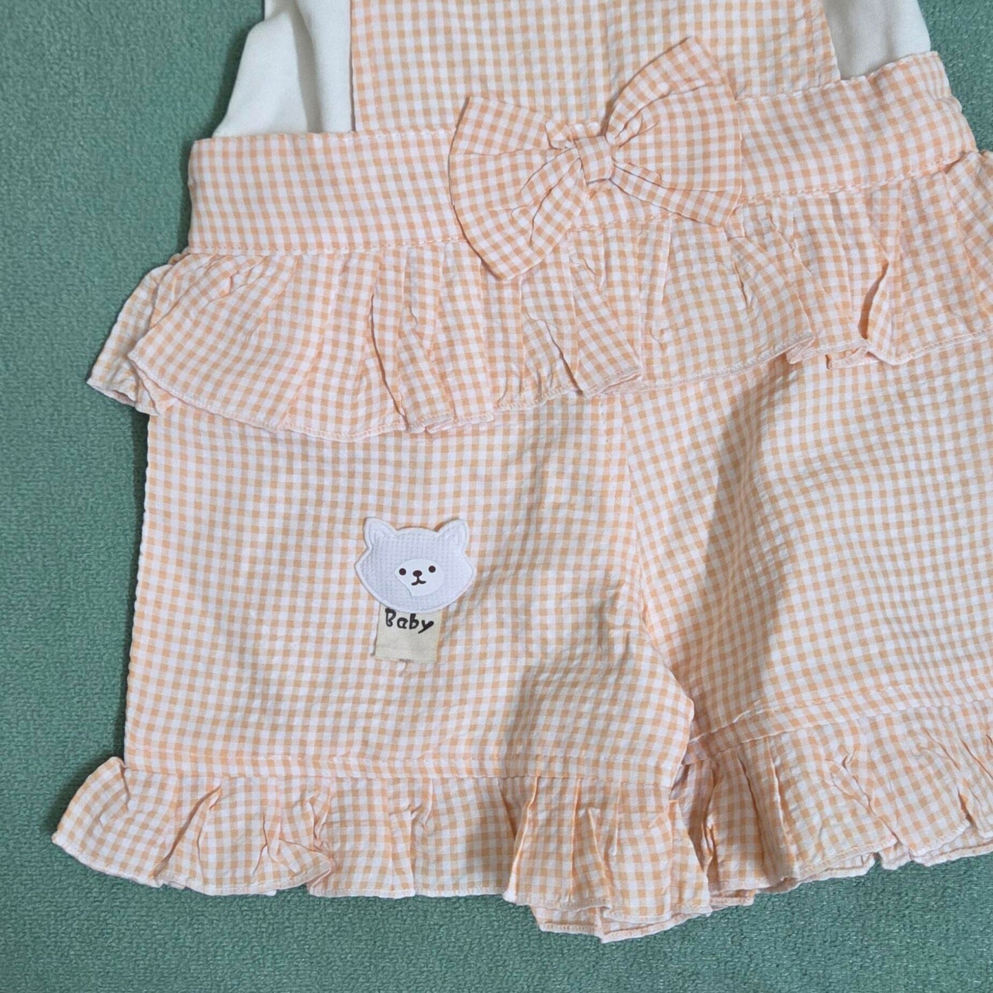 Checkered dress with ruffles and a bear emblem on a green background