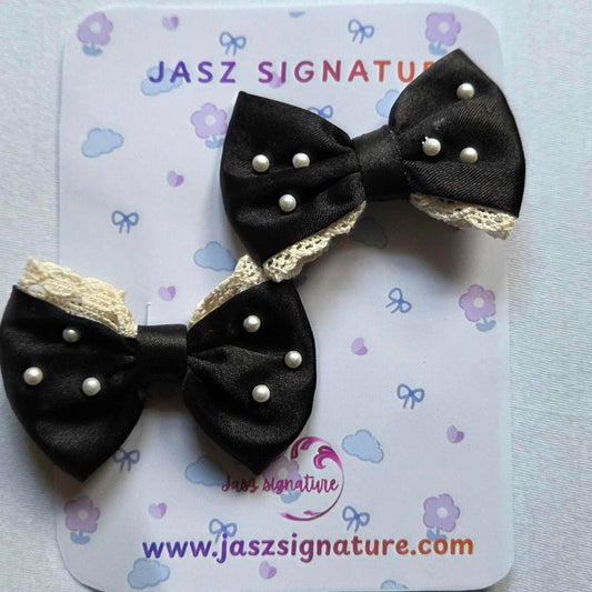 Black bow hair clips with gold accents on a Jasz Signature card.