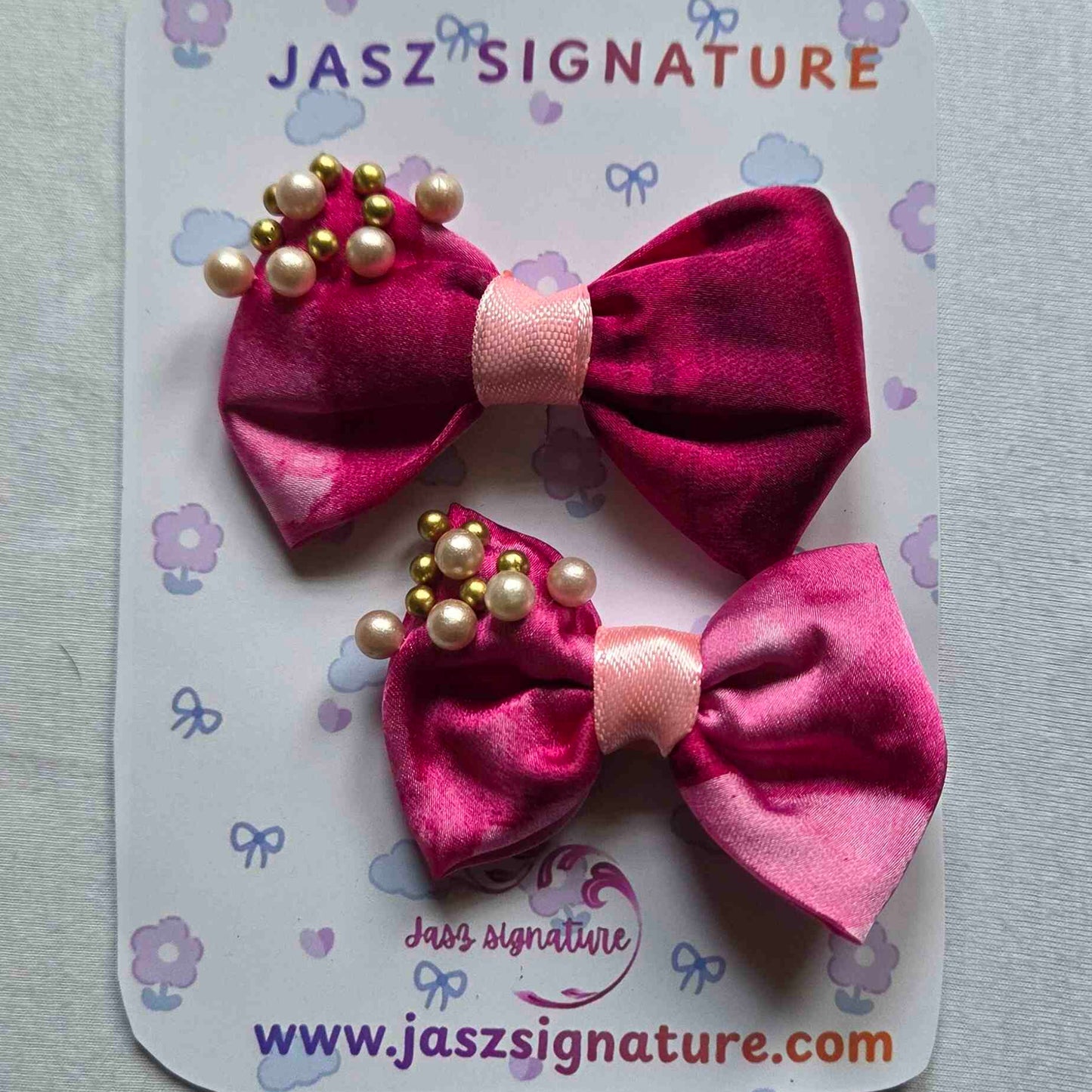 Two pink hair bows with gold beads on a Jasz Signature card.