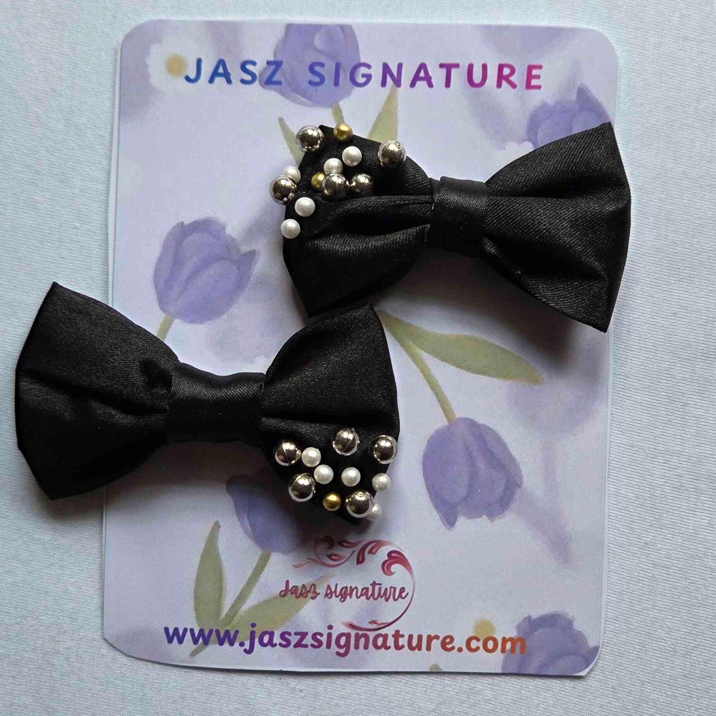 Black bow hair clip with decorative elements on a Jasz Signature branded card.
