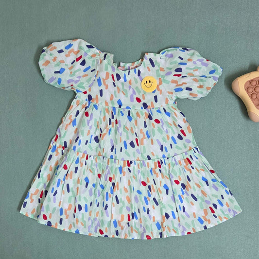 Colorful patterned dress with a smiley face button on a gray background