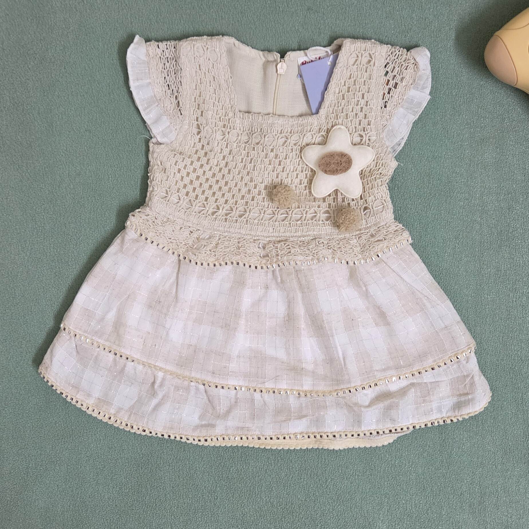 Beige baby dress with floral details on a green surface