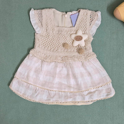 Beige baby dress with floral details on a green surface