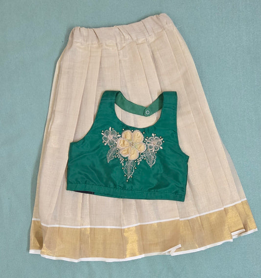 Green blouse with floral embroidery on a beige skirt with gold hem against a light blue background