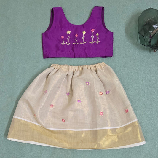 Purple blouse and beige skirt set with floral embroidery on a green background
