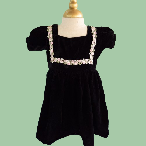 Black dress with floral embellishments on a mannequin against a green background