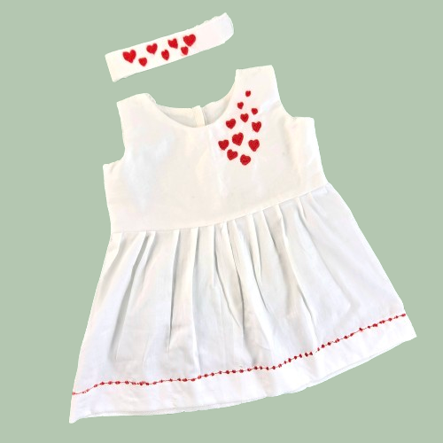 White dress with red heart patterns and a matching headband on a light green background