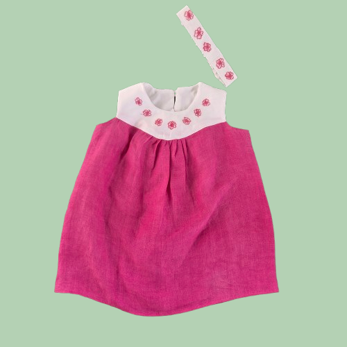 Pink dress with white collar and red floral embroidery on a light green background