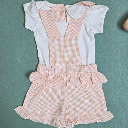 Children's outfit with pink checkered romper and white shirt on a green background
